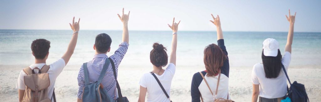 The backs of 2 males and 3 females looking out towards the beach holding up a hand sign, custom travel