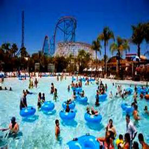 People in the pool at a water park with blue floating tubes with a roller coaster in the background