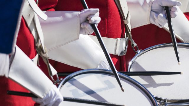 Educational Discovery Performance Tour drumline in red and white uniforms holding black drum sticks playing white drums, parades bowl games and festival tours
